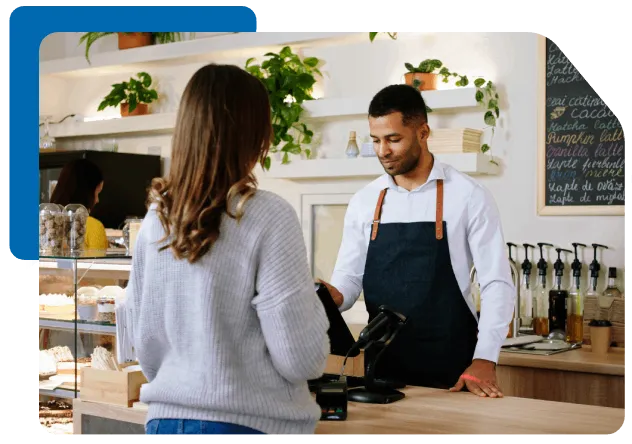 a man in a bakery shop accepting payment from a girl on his device